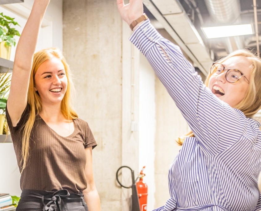 Twee teamleden steken lachend de handen in de lucht om een gezamenlijk succes te vieren.