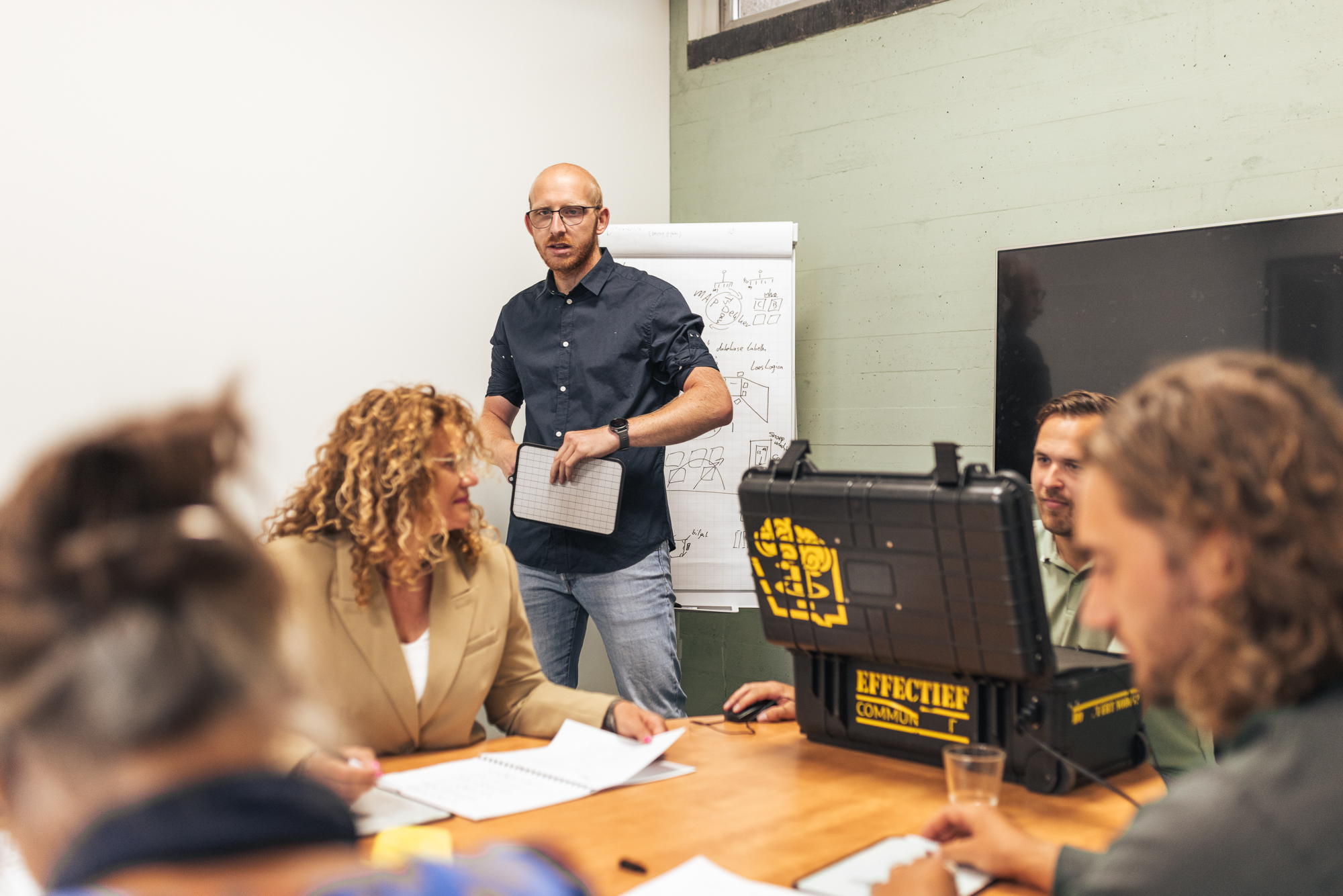 Groep speelt een serious game terwijl een trainer observeert en begeleidt.