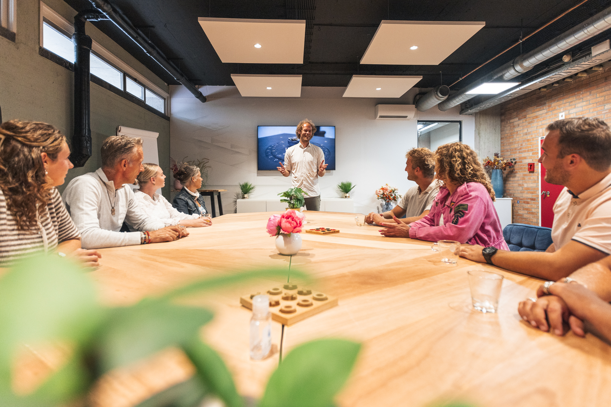 Trainer geeft uitleg aan een team tijdens een interactieve teamsessie, terwijl deelnemers aandachtig luisteren.